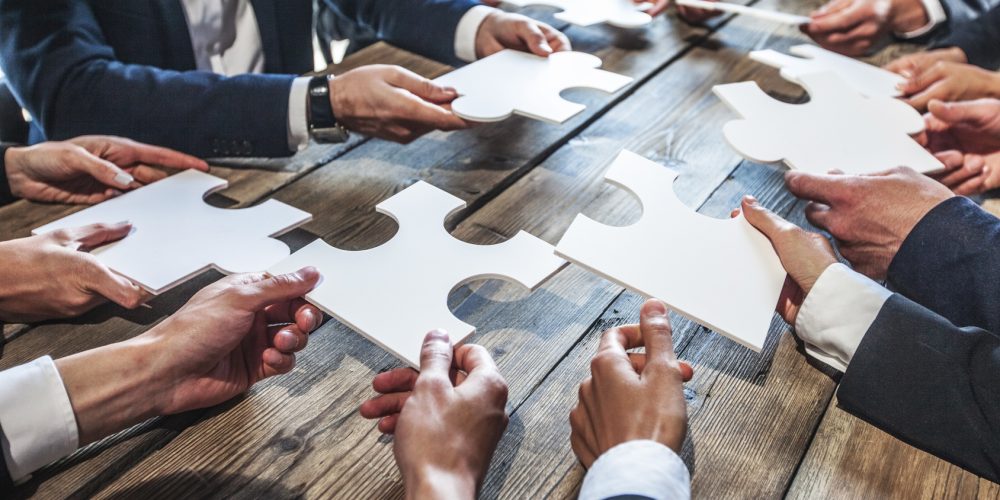 Business people and puzzle on wooden table, teamwork concept