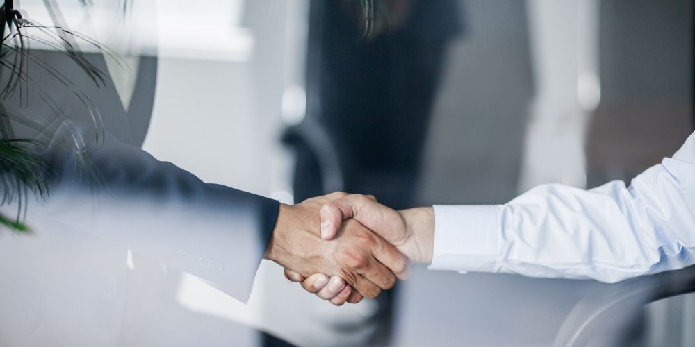 business-handshake-in-glass-reflection-in-office-675872871-31a95e1d4fd8433088e738228fd9d3dc